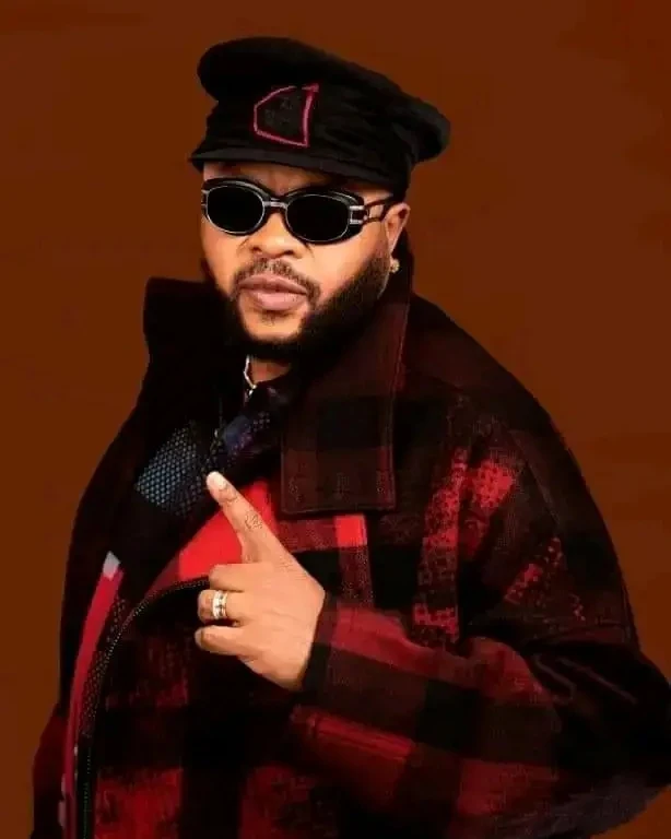 Portrait de JB Mpiana, lunettes noires et veste à carreaux rouge et noir
